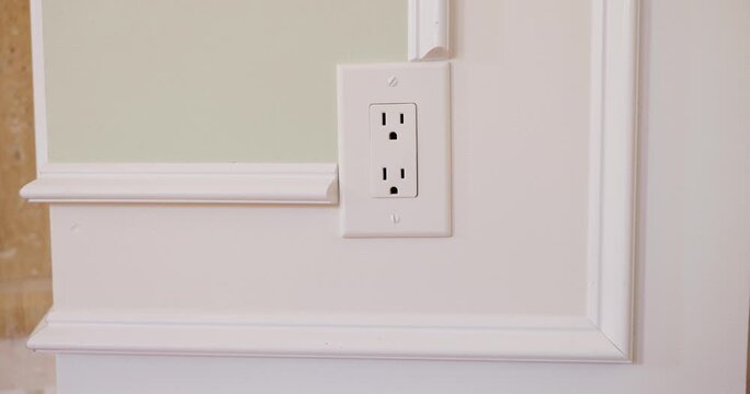 Person unplugging and plugging in black power cord to white wall outlet indoors.