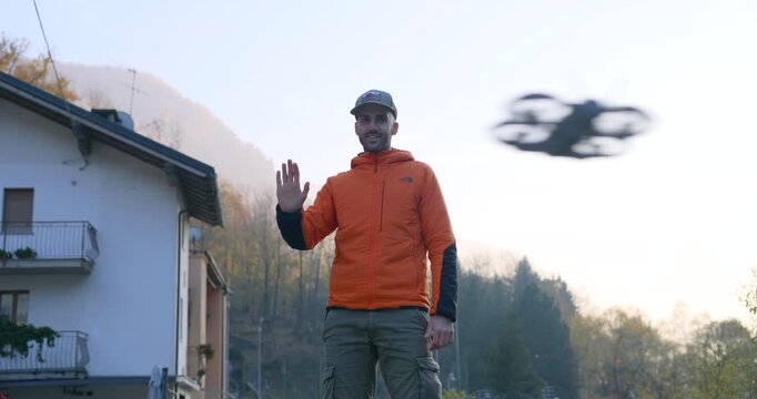 Man pilots a drone with hand gestures outdoors, controlling flight as the quadcopter hovers nearby. Modern UAV tech, intuitive motion control