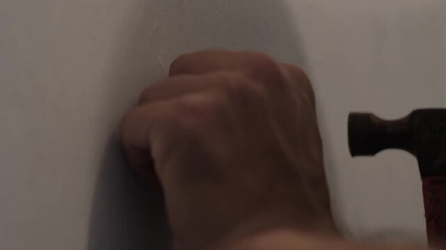 Close-up static shot of a hand inserting and hammering a wall anchor into an interior wall during installation work