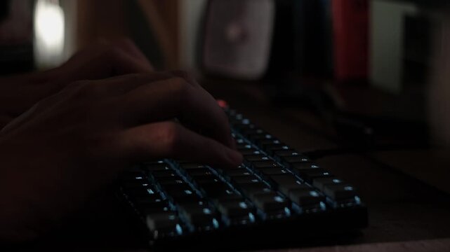 Close-up static shot of hands typing on a mechanical keyboard in a dim indoor workspace with illuminated keys and desk setup