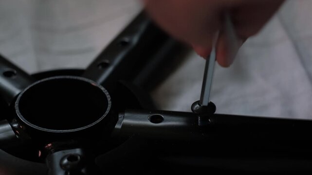 Close-up shot of hands tightening a gaming chair base with an allen wrench during furniture assembly in low light