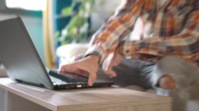 A casual freelancer in a plaid shirt replies to social media engagement with glowing floating notification icons hovering over his smartphone in a bright room.