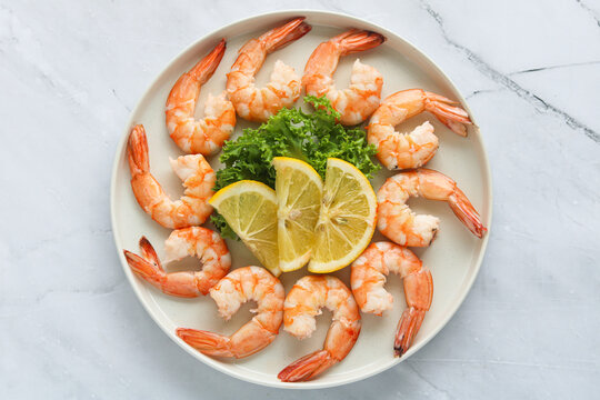 A top-down shot of several peeled and deveined cooked shrimps arranged in a circular pattern on a white plate.