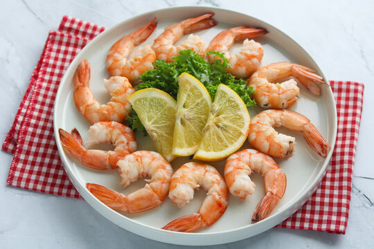 A view of several peeled and deveined cooked shrimps arranged in a circular pattern on a white plate.