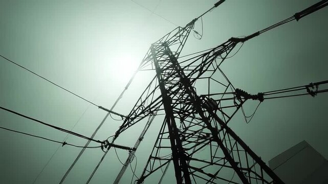 Industrial electricity transmission tower providing power and energy through high voltage lines, with a dramatic silhouette visible during foggy conditions under a bright sky