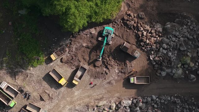 Aerial view of Tambang Pasir Merapi Kali Gendol Sand Mine with an excavator loading dump trucks near large boulders in Kecamatan Cangkringan, Daerah Istimewa Yogyakarta, Indonesia.