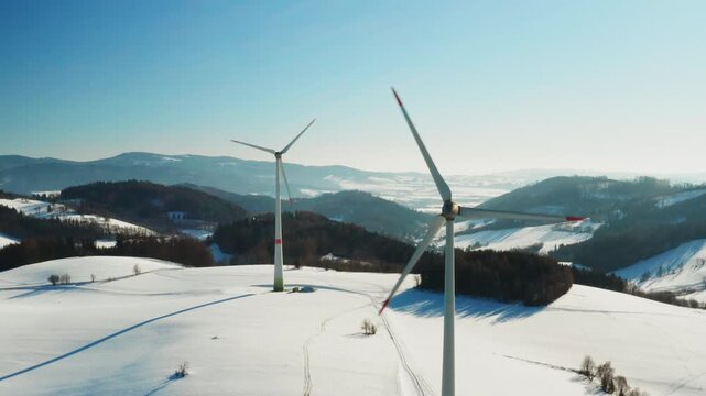 Aerial view of a single wind turbine standing in a vast snow-covered field with mountains in the background. Clean renewable energy production in a cold winter landscape 