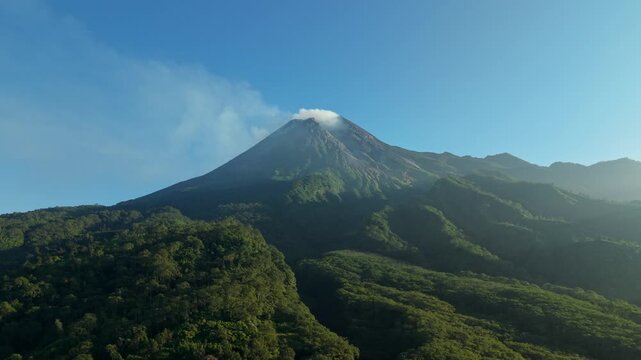 Aerial view of Mount Merapi volcano with smoke at the peak and lush green forests near Bunker Kaliadem in Kecamatan Pakem, Daerah Istimewa Yogya, Indonesia.