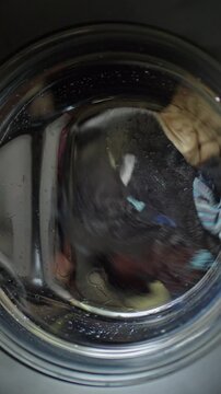 Close up view through washing machine window of clothes rotating in soapy water.