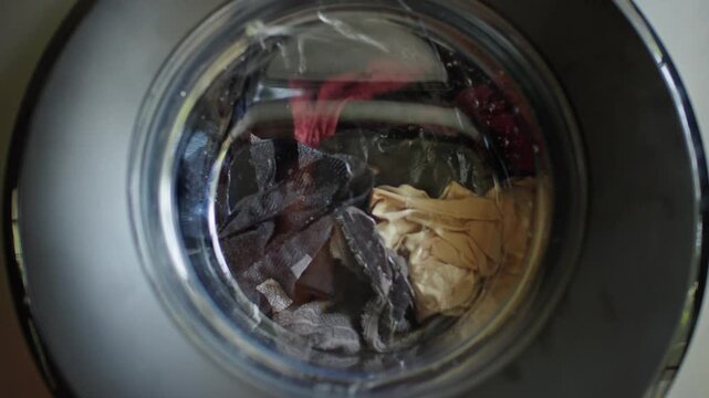 A close-up view of dirty laundry being loaded into a modern washing machine, preparing for a wash cycle.