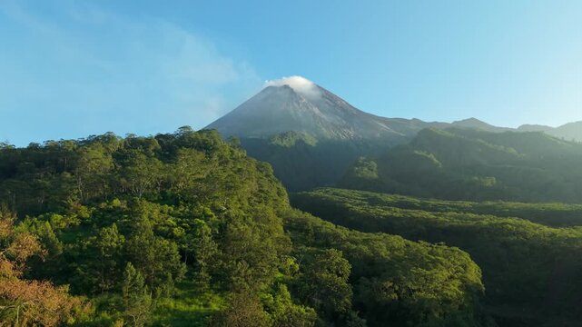 Aerial view of Mount Merapi with its smoking peak and the surrounding lush green forest near Bunker Kaliadem in Kecamatan Pakem, Daerah Istimewa Yogya, Indonesia.