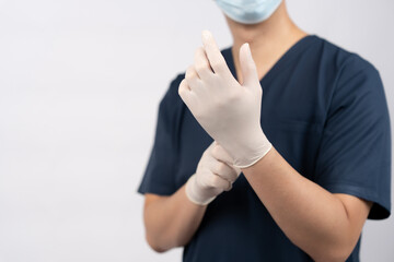 Obraz premium Asian male doctor wearing medical scrubs, surgical mask, and latex gloves in studio, representing hospital safety, healthcare services, medical technology, wellness, and patient care.