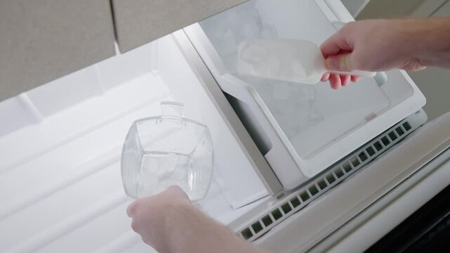 Person scoops ice cubes from freezer into a glass container, close up shot.