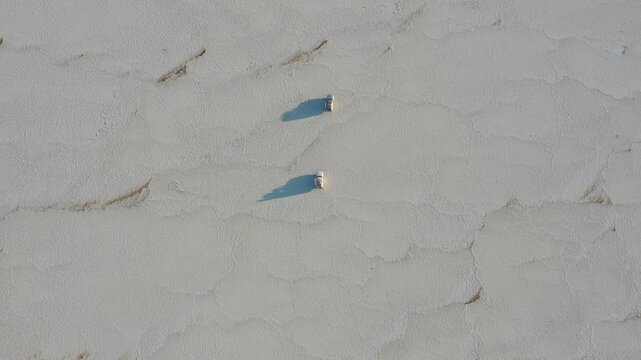 Aerial view of three off-road vehicles driving across the vast white salt flats of the Danakil Desert Dalol, Afar, Ethiopia.
