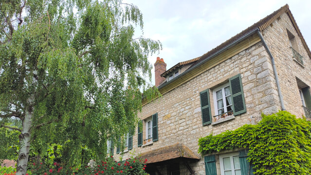 Charming Traditional French Stone House with Green Shutters, Climbing Ivy, Weeping Birch Tree, and Red Roses in Giverny Village Normandy