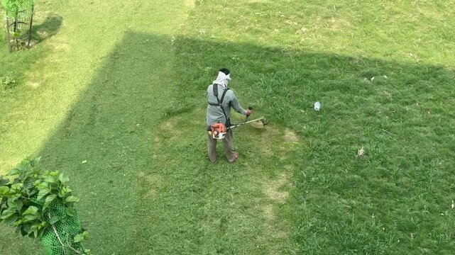 A Shot of Ground worker cutting grass with brush cutter machine in park
