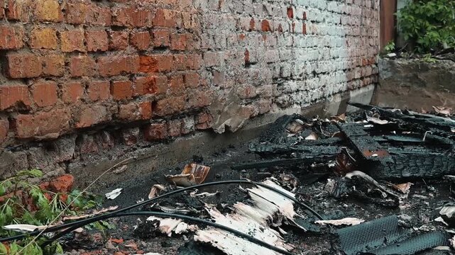Burnt debris lies scattered next to a brick wall following a recent fire incident. aftermath of the fire in an outdoor environment, highlighting the destruction caused
