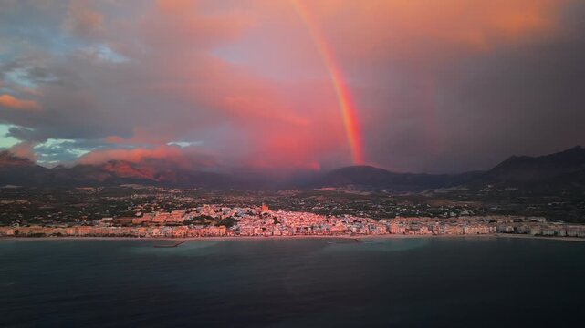 Cinematic aerial view of mediterranean coastal town with bright rainbow over altea spain at golden hour sunset.