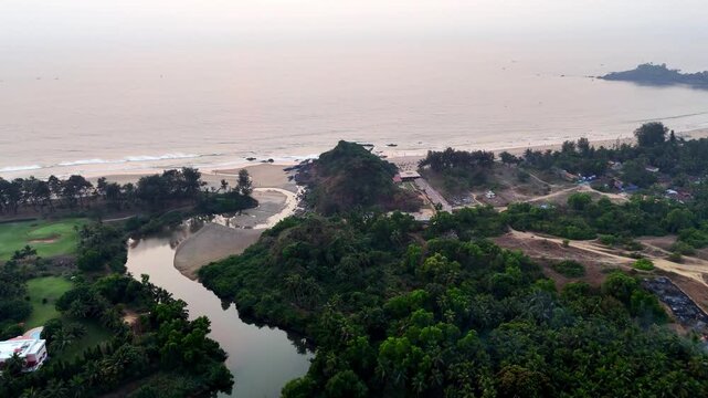 Cinematic aerial view of Canacona showcasing a winding river flowing through dense tropical greenery toward a serene sandy coastline beside the Arabian Sea.