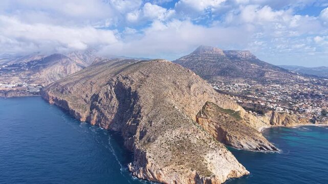 Morro de Toix cape viewpoint near Calpe, Spain, showing dramatic rocky cliffs dropping into turquoise Mediterranean Sea with coastal town and mountain backdrop