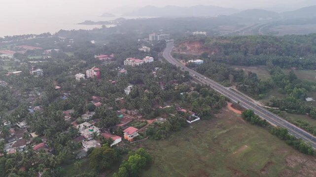 Wide cinematic foggy aerial of a highway stretching through coastal forests and rugged landscapes, blending modern infrastructure with tropical scenery, distant beaches, and mist-covered hills.