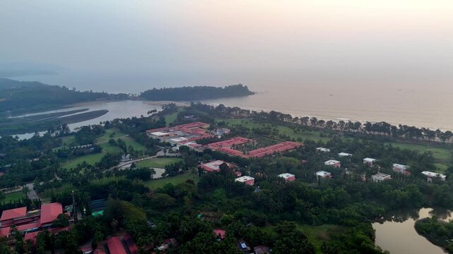 Wide cinematic aerial of Canacona highlighting expansive beachfront landscapes, landscaped resort grounds, gentle shoreline waves, and distant coastal terrain fading into soft haze.