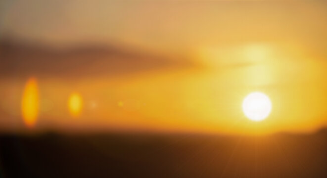 Abstract blurry sunset sky background with bright sun lens flare glowing orange yellow light soft natural bokeh effect for summer evening nature landscape design