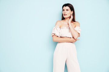 Obraz premium Young beautiful smiling female in trendy summer costume clothes. Carefree woman posing near blue wall in studio. Positive model having fun indoors. Cheerful and happy