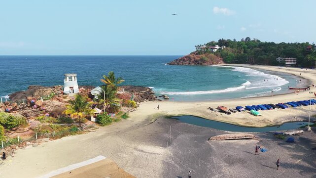 Aerial view of Kovalam beach featuring a small white tower on a rocky outcrop, palm trees, and people on the sandy shore, Kovalam, Kerala, India.