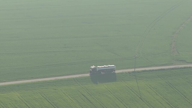 Aerial view of a tanker truck driving on a rural road surrounded by vast green agricultural fields near UGS Damborice in Damborice, South Moravian Region, Czechia.