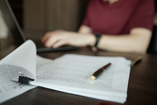 Close up of adult man typing on laptop behind script, reviewing chapters of novel 
