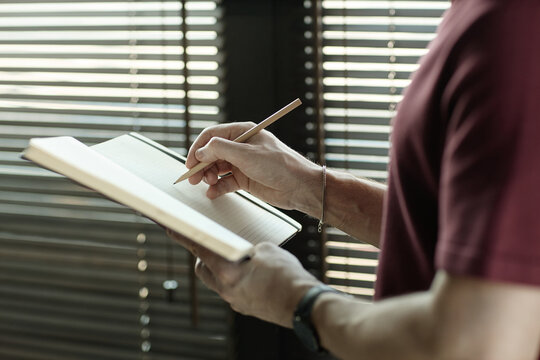 Caucasian adult man writing notes in notebook while standing indoors, capturing planning and focus
