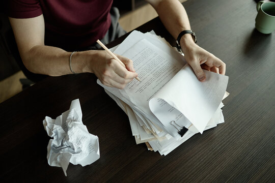 High angle view of adult man reviewing printed novel chapter and making edits at desk