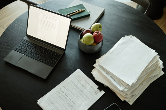 High angle view of laptop displaying document beside printed pages and notes on table, supporting editing workflow and manuscript review for publishing or remote work
