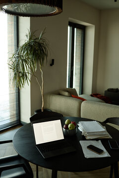 Vertical shot of laptop displaying document beside paperwork and smartphone on dining table in home office, supporting remote work, productivity, planning
