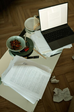 Laptop, pages on new novel and plates with breakfast placed on kitchen counter 
