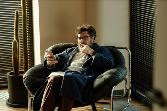 Caucasian author sitting in chair and looking at smartphone screen while checking social networks 