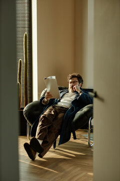 Vertical shot of middle aged Caucasian man reviewing novel while sitting in chair