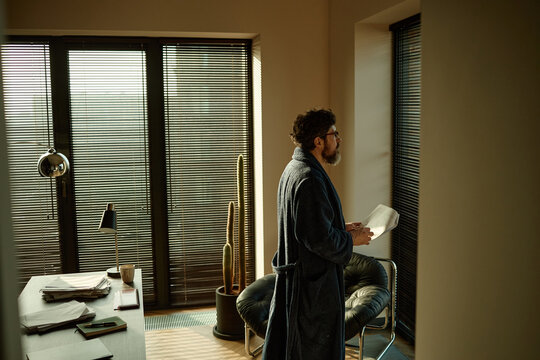 Middle aged Caucasian writer reading printed chapters of novel while working at home

