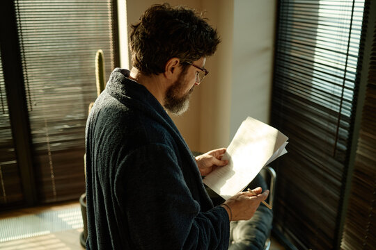 Middle aged Caucasian man standing still in center of home office, reading novel and checking spelling
