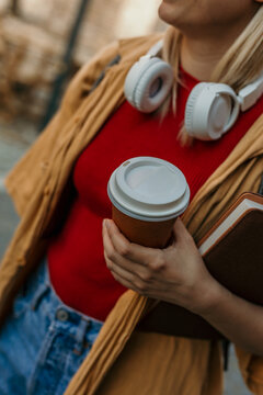 Student holding coffee cup and book with headphones around neck