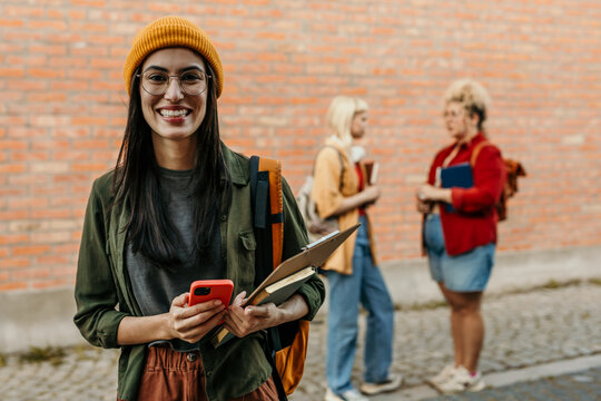 Young smiling female student holding phone and books