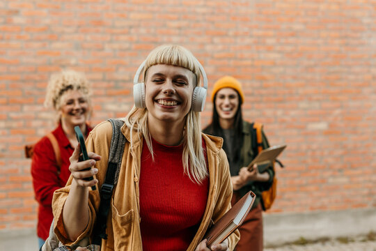 Happy student wearing headphones enjoying music with friends