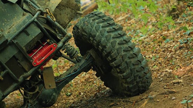 Rugged off road vehicle detail. Muddy tire, axle, and suspension navigate difficult forest trail. Red winch highlights extreme motor sport competition. Concept of power and adventure