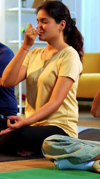 Indian young family doing meditation pranayama at home practicing breathing exercise together indoors during peaceful morning hours in a modern lavish living room promoting yoga health wellness