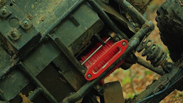Close up of red recovery winch with synthetic rope on custom off road buggy. Muddy frame and suspension show signs of extreme competition in forest terrain. Rugged and powerful machinery