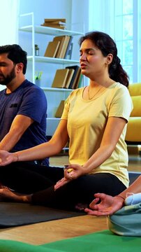 Indian young family doing omkar meditation pranayama at home chanting aum breathing yoga together indoors during peaceful morning hours in a modern living room promoting yogic lifestyle