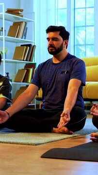 Indian young family doing omkar meditation pranayama at home chanting aum breathing yoga together indoors during peaceful morning hours in a modern living room promoting yogic lifestyle
