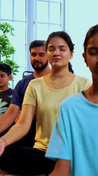 Indian young family doing omkar meditation pranayama at home chanting aum breathing yoga together indoors during peaceful morning hours in a modern living room promoting yogic lifestyle