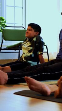 Indian family doing yog asana at home relaxing legs between yoga session while sitting on floor together indoors during calm morning hours in modern lavish living space promoting healthy lifestyle